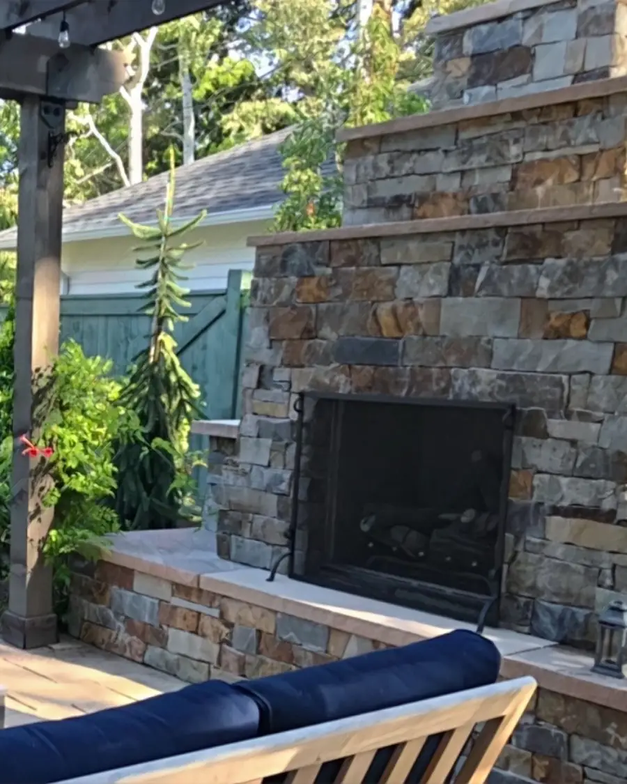 Stone outdoor fireplace under a pergola with seating